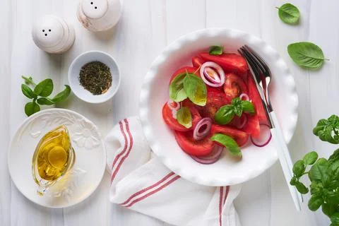 Fresh tomatoes salad with basil leaves, olive oil and onion in white bowl on  Stock Photos