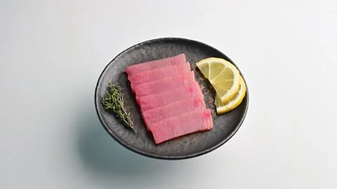 Fresh tuna slices served on a black plate with lemon and thyme garnish for a Stock Footage 305229760