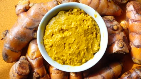 Fresh turmeric paste in white bowl with whole roots scattered on vibrant ye.. Video stock 332879633