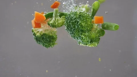 Fresh vegetables falling under water on white background in slow motion. Salad Stock Footage 107380967