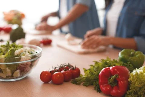 Fresh vegetables on the kitchen table with couple preparing food on the backg Stock Photos