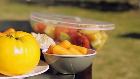 Fresh vegetables sitting on plates next to a smoking barbeque in the sunshine. Stock Footage 88341954
