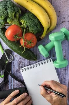 Fresh vegetables, two hands and a notepad, dumbbells and elastic, healthy l.. Stock Photos