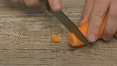 A fresh, vibrant carrot and a sharp knife resting on a rustic wooden surface for Stockbeeldmateriaal 280605612