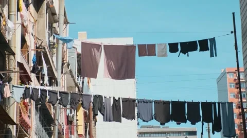 Fresh washed clothes drying on clothesline between buildings against blue sky Stock Footage 272817236