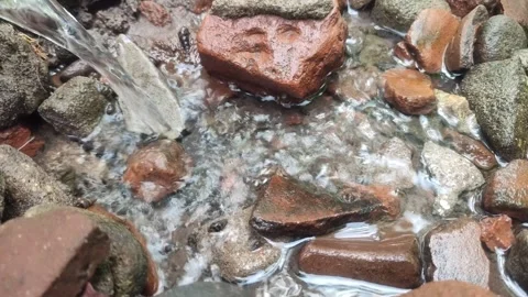 Fresh water flows gently over a pile of natural stones and red bricks Stock Footage 309788232