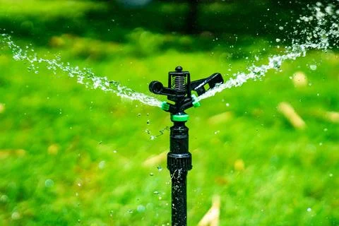 Fresh water splash from the sprinkle pole settle in the grass feild in the .. Stock Photos