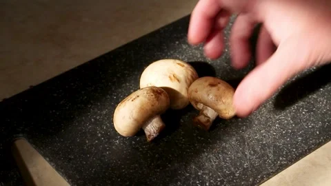 Fresh white mushrooms being placed on black cutting board for food preparation Stock-Footage 335540883