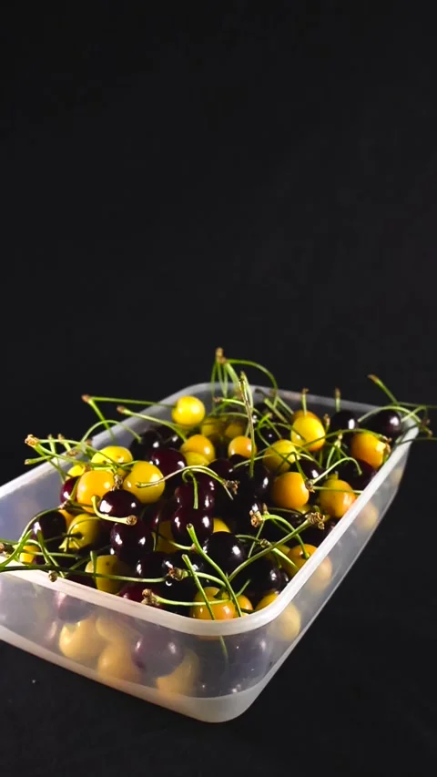 Fresh yellow and red cherries in a plastic container on black background Stock Footage 340146246