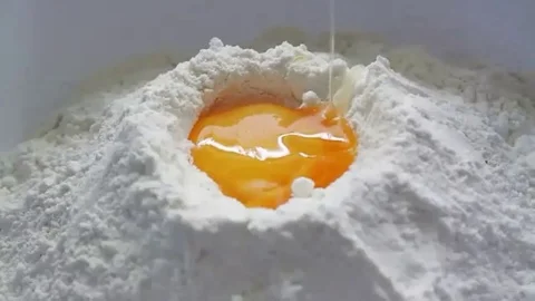 Fresh yellow egg being broken and dropped down into white baking flour Stock Footage 98247573