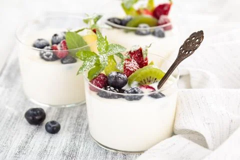 Fresh yogurt with berries. On white rustic table. Focus on mint leaves and ki Stock Photos