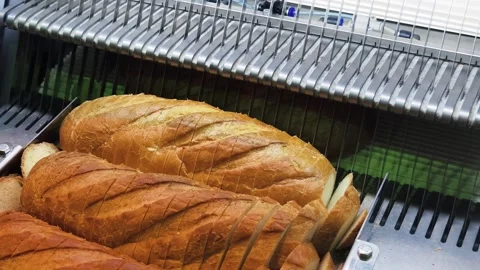 Freshly baked bread being sliced in a bakery using a commercial bread slicer Stock Footage 306296042