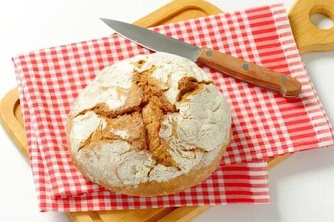 Freshly baked bread with knife on checkered cloth Stock Photos