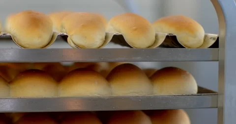 Freshly baked bread rolls resting in metal trays on bakery rack with warm Stock Footage 344583298