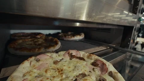 Freshly baked pizzas being removed from a commercial oven, showcasing the golden Stock Footage 332736681