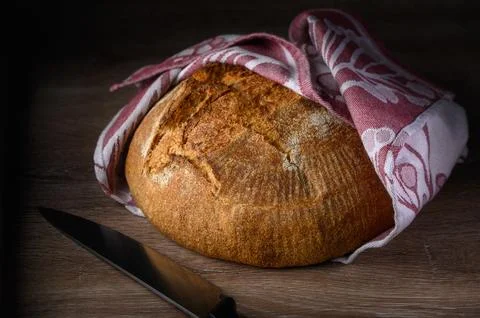 Freshly baked round bread wrapped in a cozy cloth on a wooden surface Foto stock