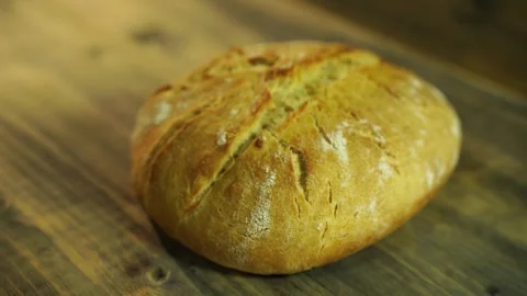 Freshly baked round loaf of bread lies on a wooden table Stock Footage 284953991