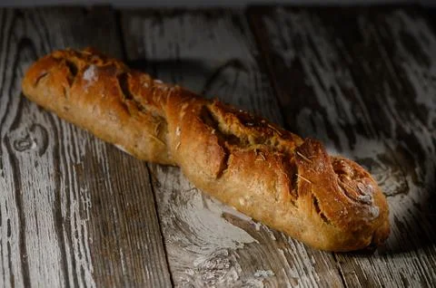 Freshly baked rustic bread loaf resting on an aged wooden table illuminated Stock Photos