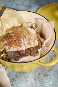 Freshly baked rustic bread in yellow cast iron Dutch oven Description: Stock Photos