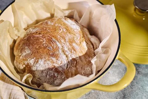 Freshly baked rustic bread in yellow cast iron Dutch oven Description: Stock Photos