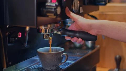 Freshly brewed coffee flows in a thin stream from the coffee machine into a Stock Photos