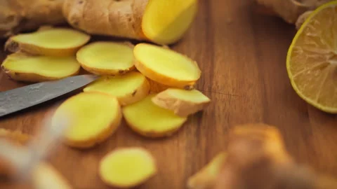 Freshly chopped ginger root and a lemon wedge rest on a worn wooden cutting Stock Footage 331353445