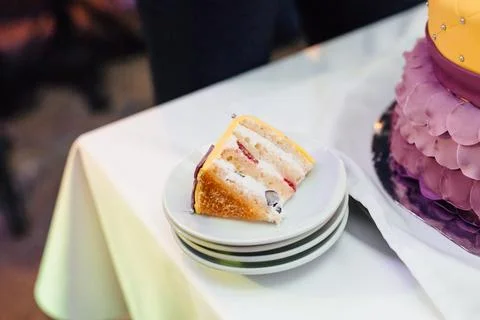 Freshly cut slice of fruit sponge cake on stacked white plates beside a Stock Photos