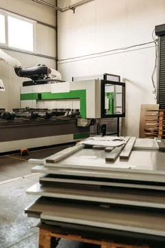 Freshly cut wood panels stack next to a CNC router in a bright factory. The m Stock Photos