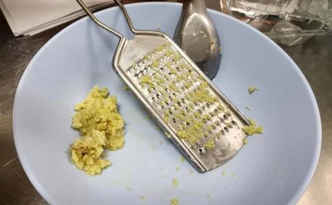 Freshly Grated Ginger Root in a Blue Bowl with a Stainless Steel Grater Stock Photos