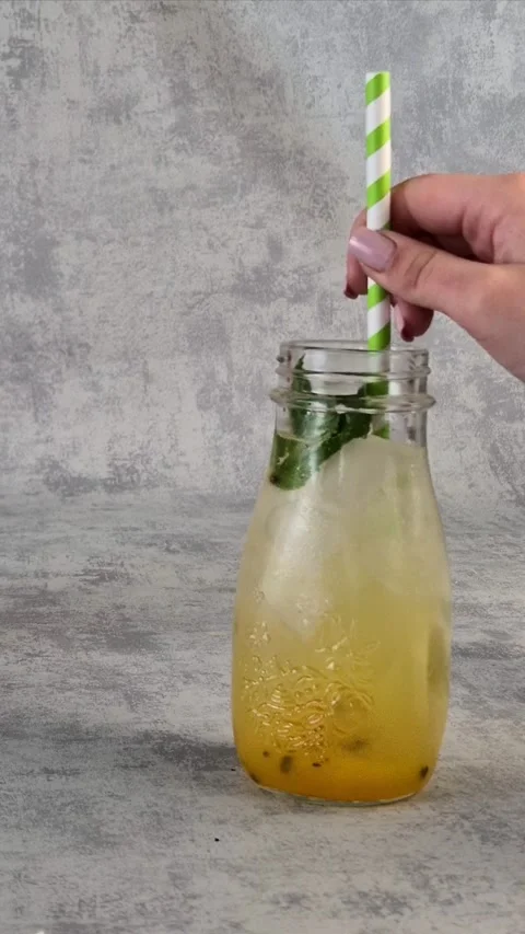 Freshly made passion fruit mango lemonade in a glass with ice. A female hand  Stock Footage 304741031