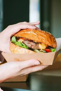 Freshly prepared cheeseburger in a paper box. Takeaway or delivery concept. Stock Photos