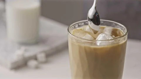 Freshly prepared cold coffee ice cocktail with milk mixing by spoon. Stock Footage 129638416