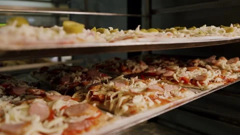 Freshly prepared pizzas with various toppings placed on metal trays inside a Stock Footage 340172367