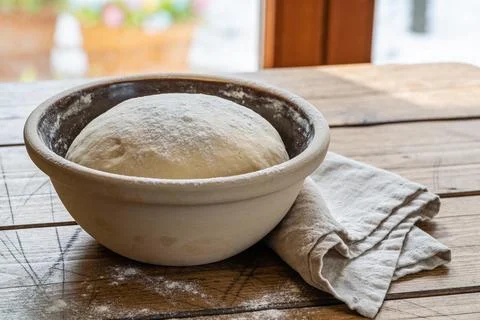 Freshly risen bread dough dusted with flour in a rustic bowl on a wooden tabl Stock Photos