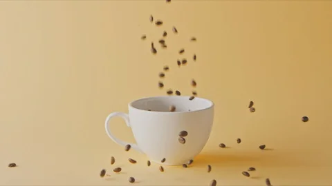 Freshly roasted coffee beans is fulling ceramic cup and fall around. Stock Footage 129634995