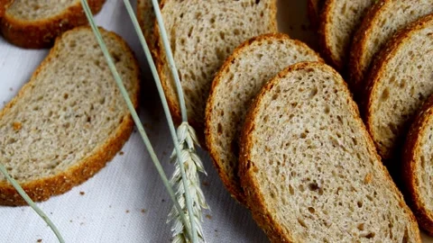 Freshly sliced whole grain bread arranged on a white cloth with stalks of wheat Stock Footage 336322823