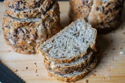 Freshly sliced whole grain bread with nuts and seeds on wooden cutting board Stock Photos