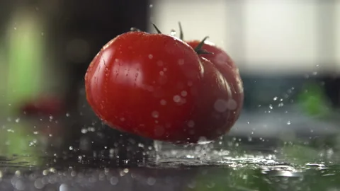 Freshly washed beefsteak tomato fall in slow motion onto a shiny slate board. Video stock 160927514