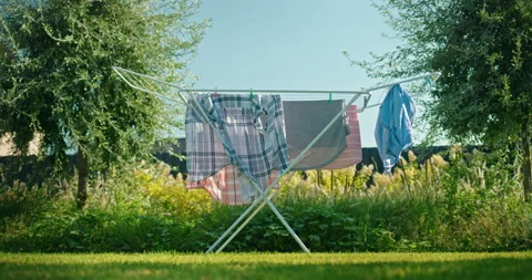 Freshly washed clothes drying on a folding rack under the sun in a green Vídeos de archivo 308941152