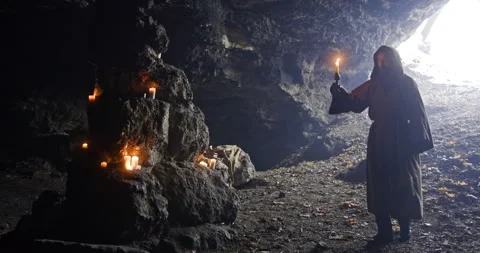Friar with a candle in his hands wanders in a large dark cave on a background of Video stock 171487375