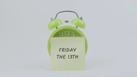 Friday the 13th word on sticky note in front of green clock and ringing Stock Footage 313985310