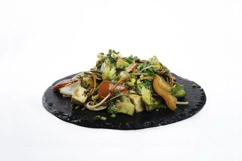 Fried assorted vegetables with meat in a flat plate on a white background, side Stock Photos