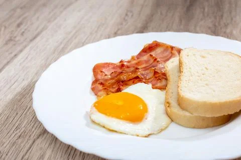 Fried bacon with egg and bread on a white plate Stock Photos