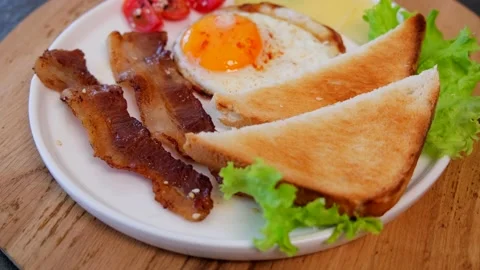 Fried bacon with eggs, toasts, cherry tomatoes, and cheese on a white plate. Stock Footage 154236686