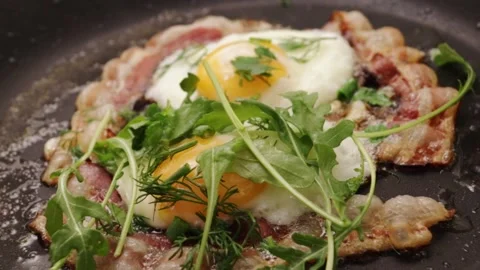 Fried bacon strips with eggs sizzling in a hot pan with fresh herbs Stock Footage 252021262