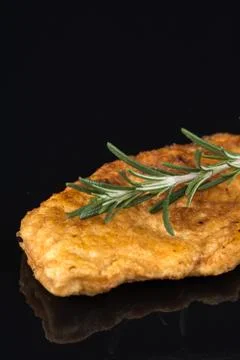 Fried breaded chicken white meat with rosemary branch above black background  Stock Photos