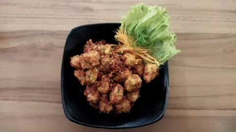 Fried chicken bites with crispy coating and lettuce garnish served in a black Stock Photos