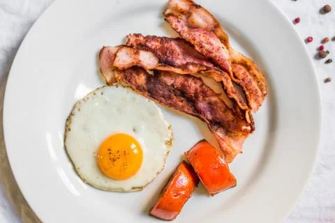 Fried chicken eggs with crispy bacon and tomatoes against white background Stock Photos