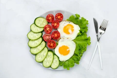 Fried chicken eggs with vegetables on a gray table. Breakfast concept. Top vi Stock Photos
