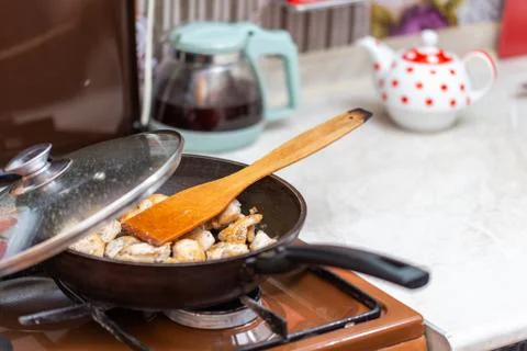 Fried chicken in a open pan with ground black pepper and wooden kitchen spatula Photos